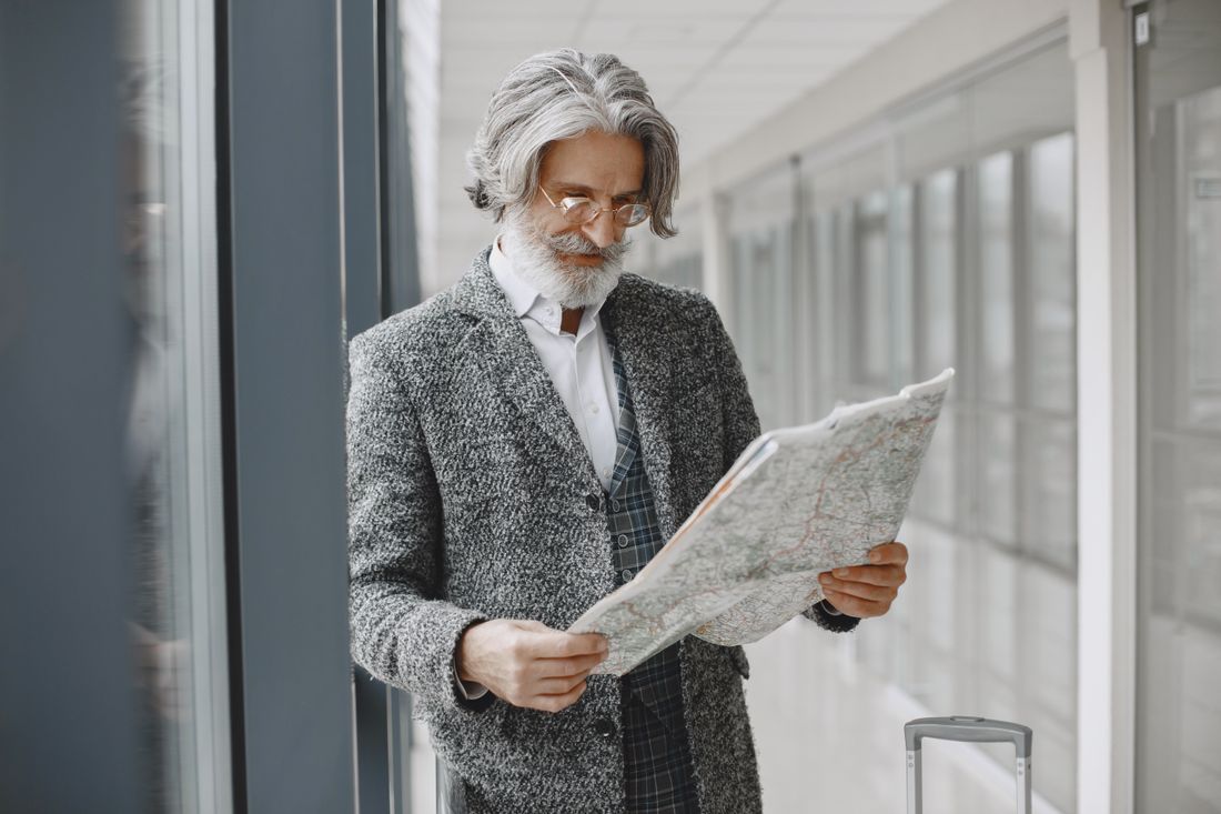 An older traveler with a suitcase reading a map in an airport walkway