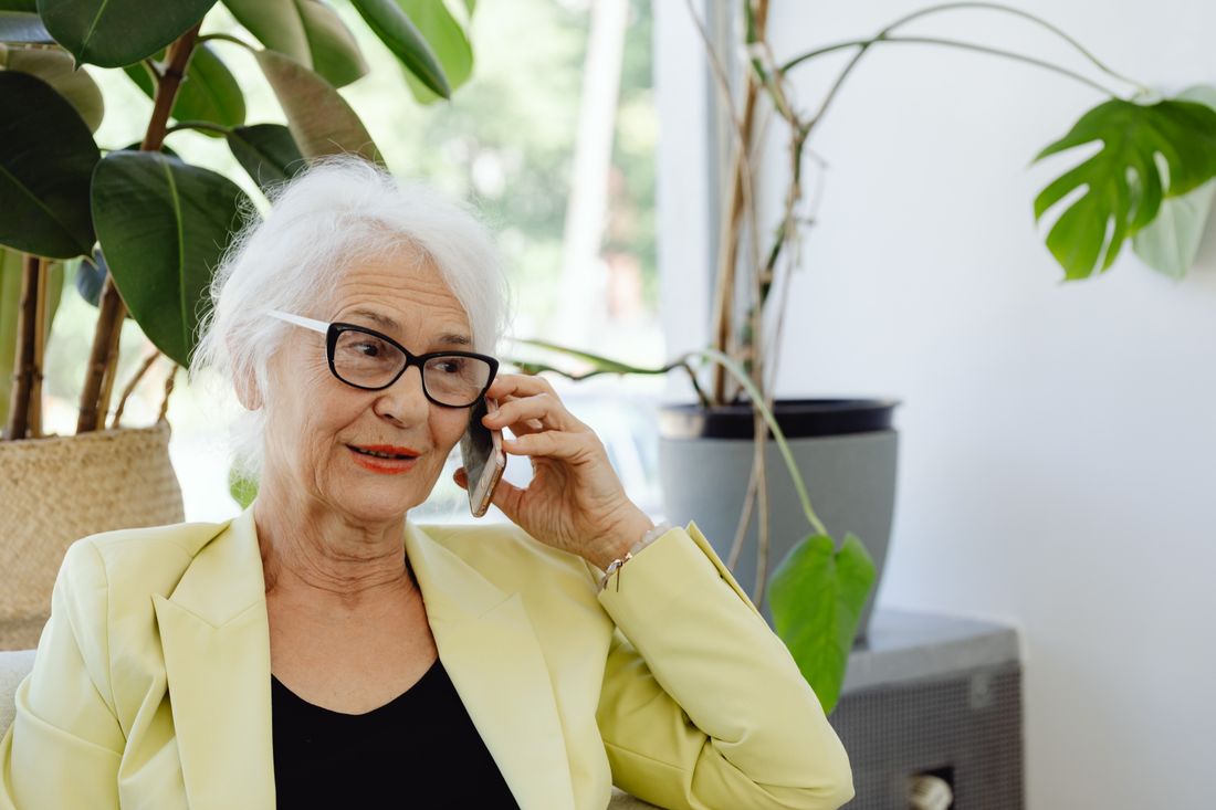 A smiling older woman with glasses talking on the phone at home